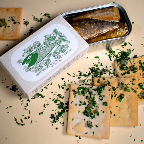 conserve de sardines fumées à l'huile d'olive sur une table beige avec cracottes et persil