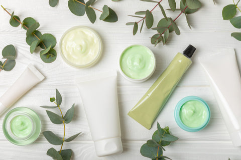 produits de soin, crèmes et cosmétiques sur une table en bois blanche entourés de feuilles vertes
