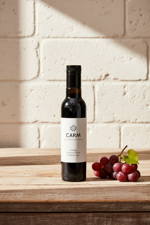 bouteille en verre noir de vinaigre de vin sur une table en bois, fond en pierre blanche, raisins rouges sur le côté droit