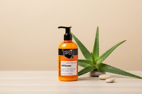 conditioner orange en flacon pompe sur une table en bois clair sur un fond beige clair, pierres et aloe vera à droite du récipient