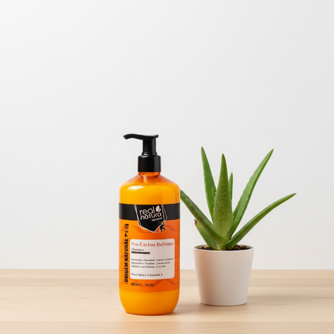 shampoing orange en flacon pompe sur une table beige clair sur fond blanc avec un pot d'aloe vera à droite du récipient